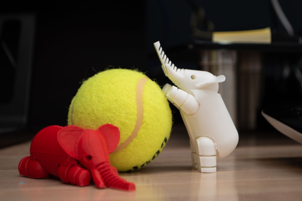 Two 3D-printed elephant figures posed next to a tennis ball.